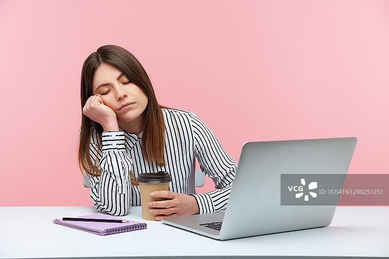 困倦低效的女办公室职员倚着头，拿着咖啡杯，坐在工作场所，手提电脑，身体疲惫图片素材