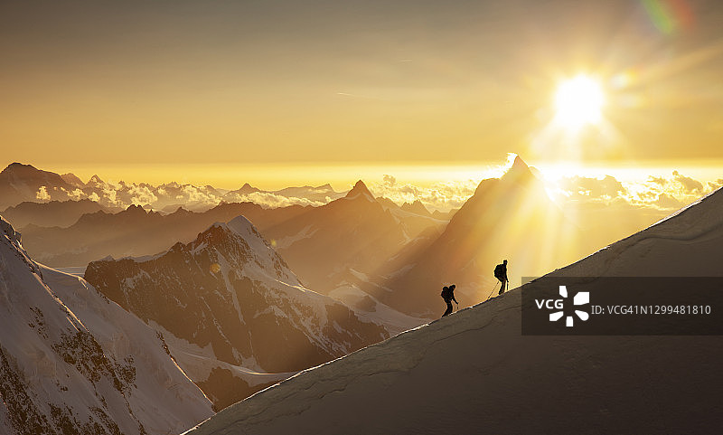 日出时，攀登者在白雪皑皑的山脊上图片素材