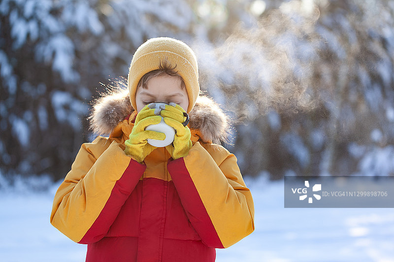 孩子喝热巧克力或可可在下雪的冬天公园。图片素材