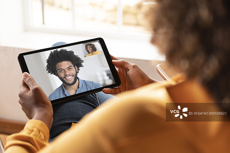 一名女子坐在家里通过数字平板电脑与一名微笑的男子进行视频通话图片素材
