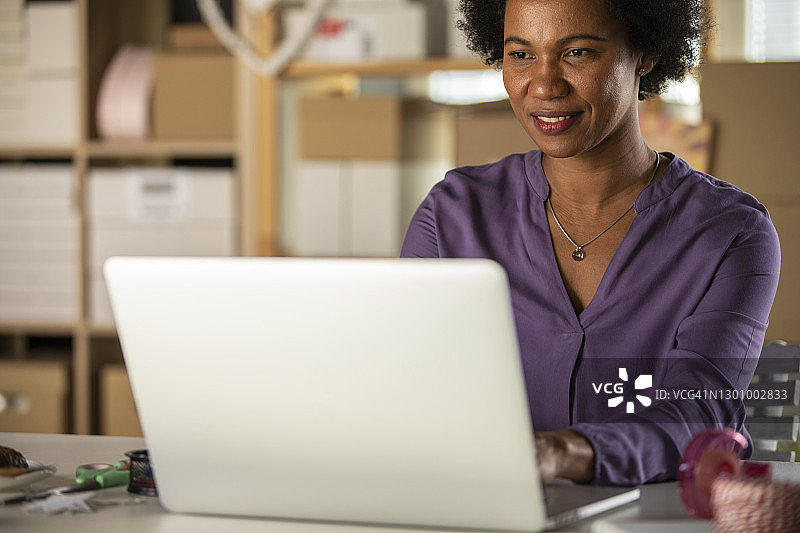 微笑的非洲裔美国妇女坐在她的桌子和使用笔记本电脑图片素材