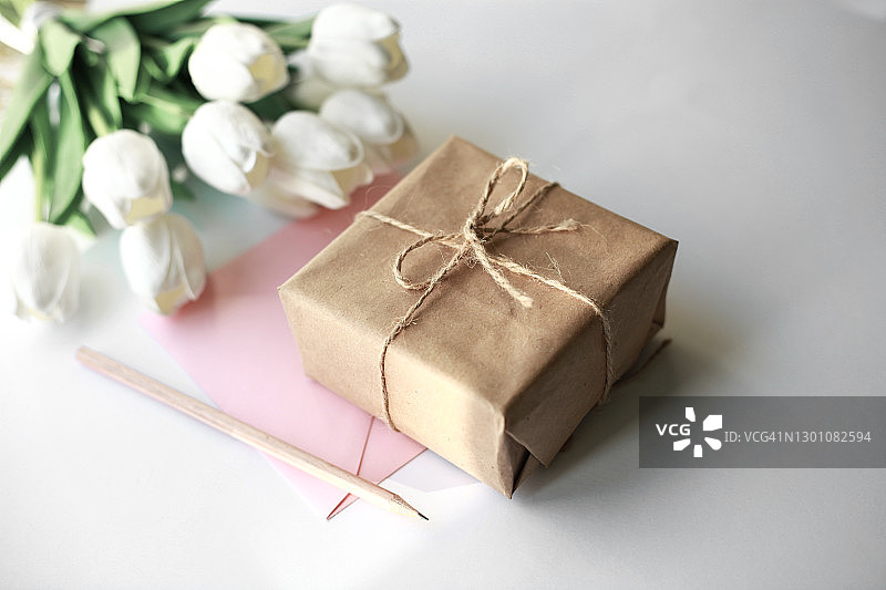 白色郁金香花和工艺礼品盒在柔和的白色背景。贺卡与复印空间。图片素材
