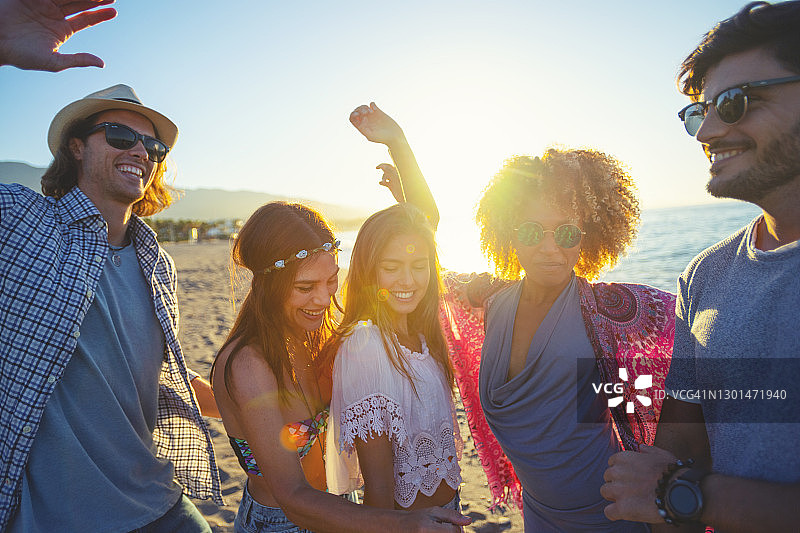 一群朋友在沙滩上跳舞庆祝日出/日落。图片素材