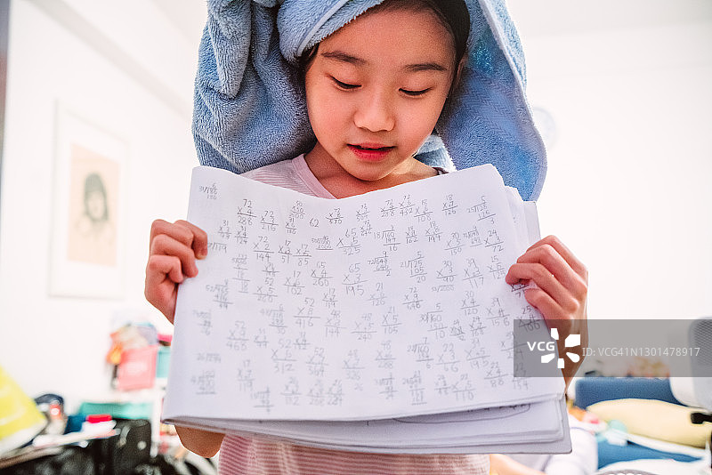 可爱的女孩展示她手写的数学计算在一个笔记本在家里的相机图片素材