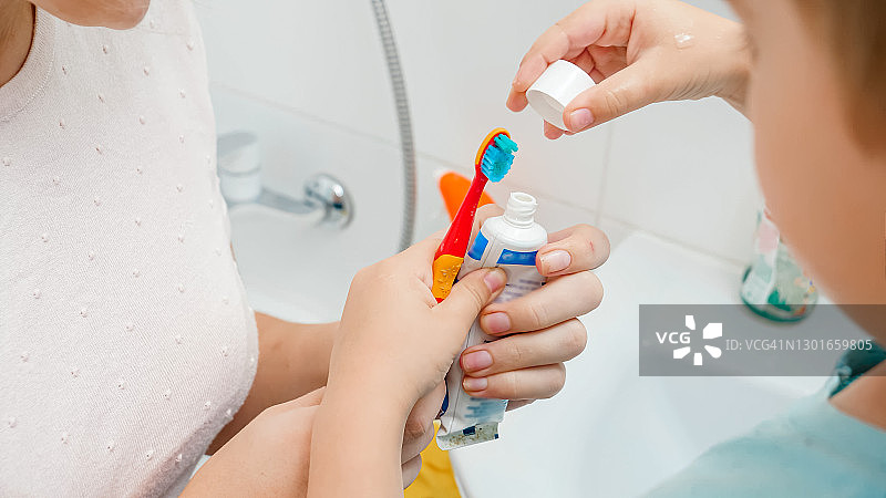 母亲帮助她蹒跚学步的儿子涂抹牙膏的特写。儿童使用牙刷和牙膏刷牙和清洁牙齿图片素材
