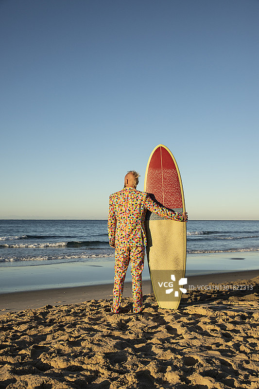 穿着西装的人拿着冲浪板站在海滩上图片素材