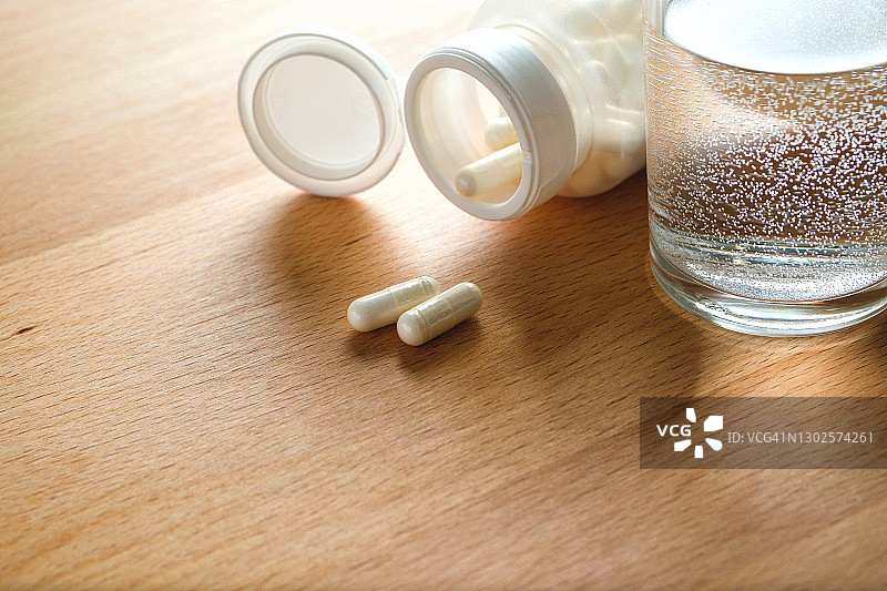 药片和一杯水放在厨房的木制桌子上。服用维生素、止痛药、药物和膳食补充剂。疾病的概念预防和治疗，保健和医药。计划和准备怀孕。图片素材