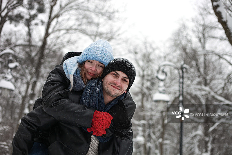 快乐的年轻夫妇男人和女人拥抱和有乐趣的户外在冬天在下雪的天气图片素材
