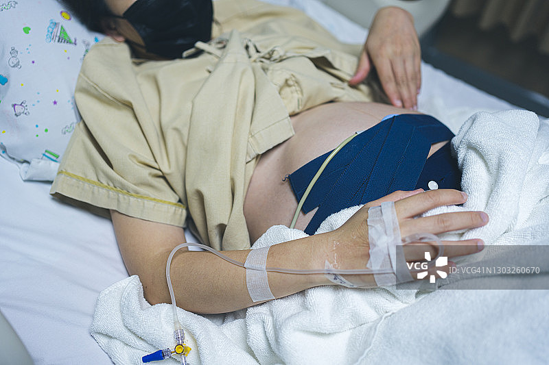 亚洲母亲睡在床上，在分娩前用心率带监测器检查婴儿的脉搏图片素材