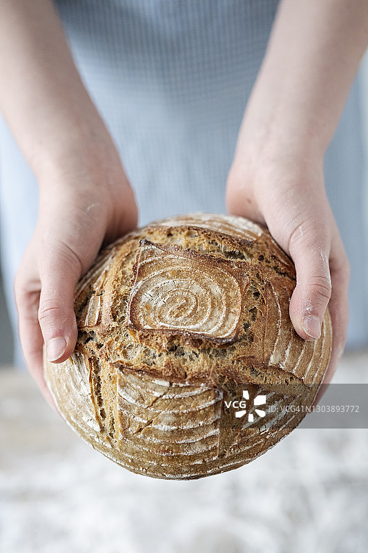 面包师拿着一个刚烤好的圆面包。图片素材