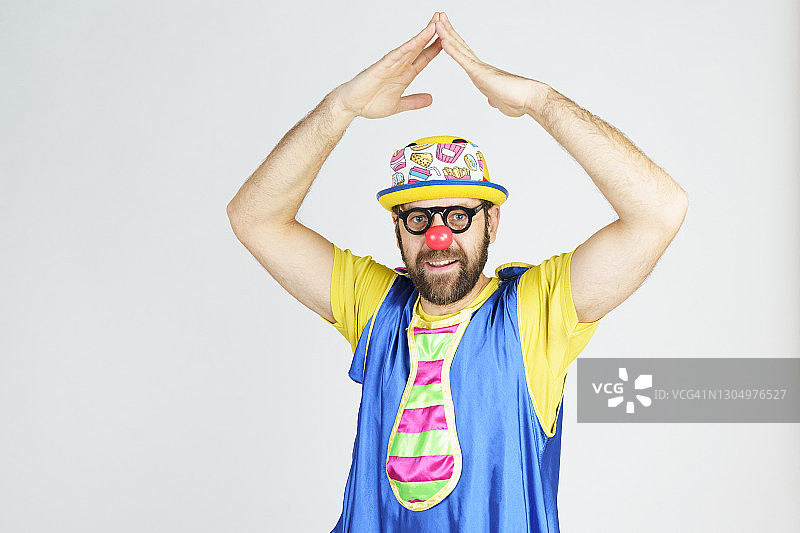 小丑——一个穿着亮蓝色和黄色衣服，戴着眼镜和帽子的男人情绪激动地举起了他的双手。图片素材