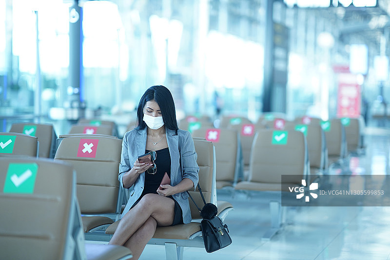 在机场，一名年轻女子坐在分开的椅子上发手机短信图片素材