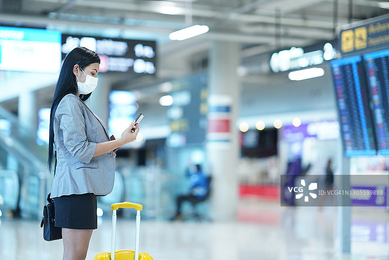 年轻女子站在机场出发区，一边聊天一边发短信图片素材