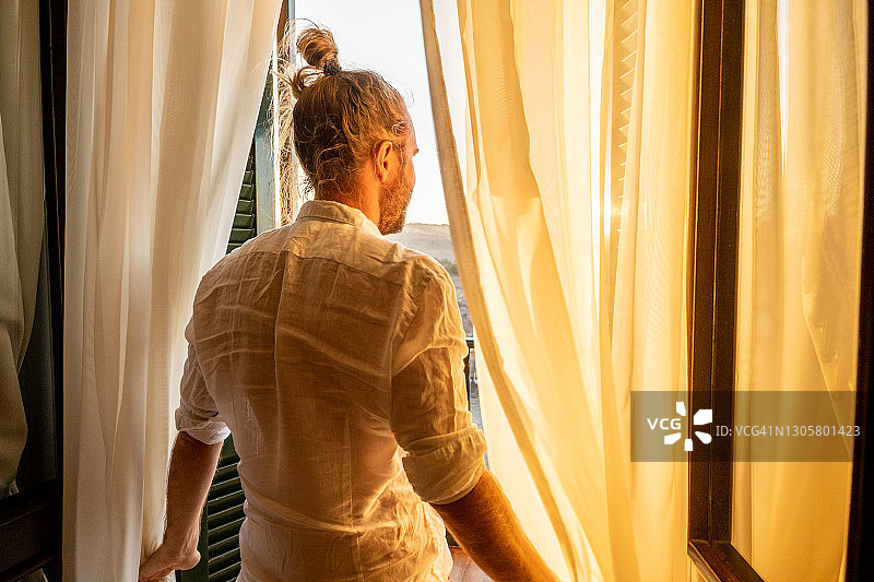 日出时分，尼罗河上，一名男子在酒店房间拉开窗帘图片素材