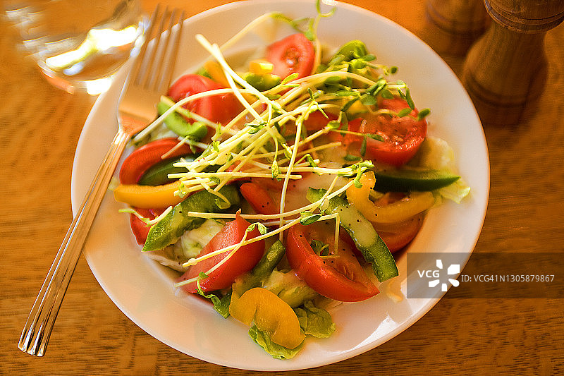 新鲜的春天，蔬菜沙拉与番茄，辣椒和豆芽在一个沙拉盘在木桌子上与叉木盐和胡椒研磨图片素材