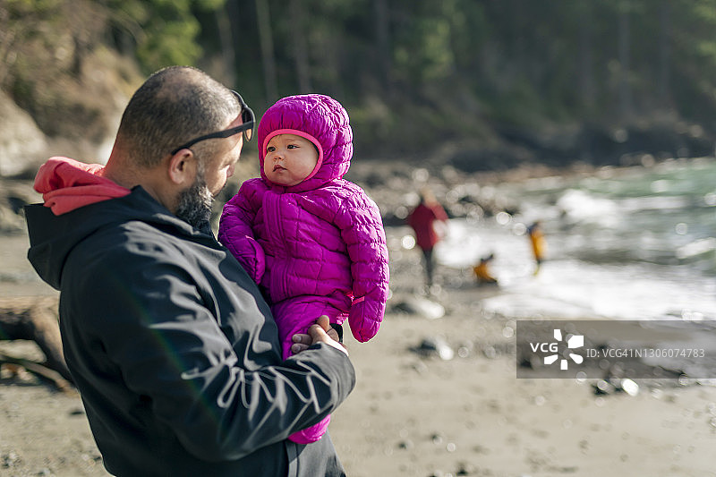 快乐的父亲抱着蹒跚学步的女儿在海滩上图片素材