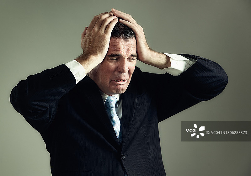 头痛或苦恼:一名西装男子抬起头，看上去非常不安图片素材