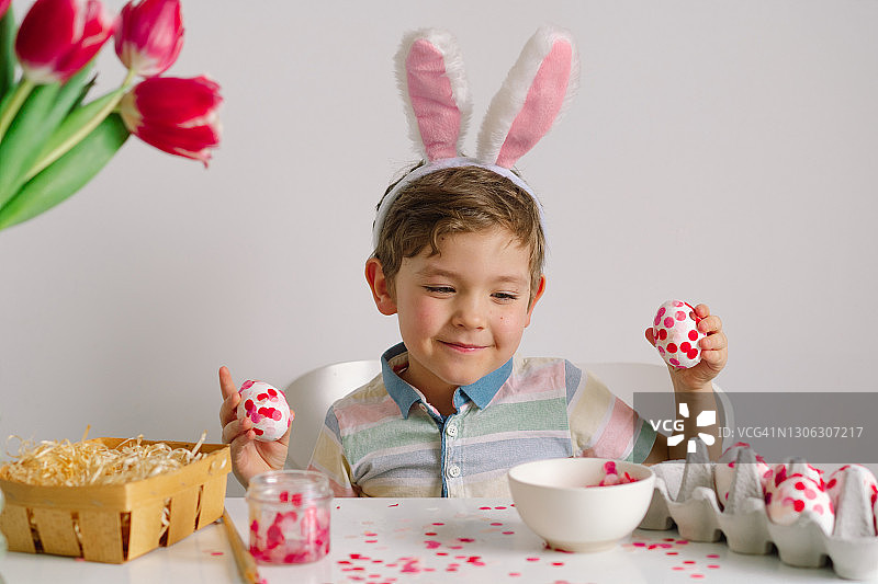 戴着兔子耳朵的小男孩装饰复活节彩蛋。图片素材