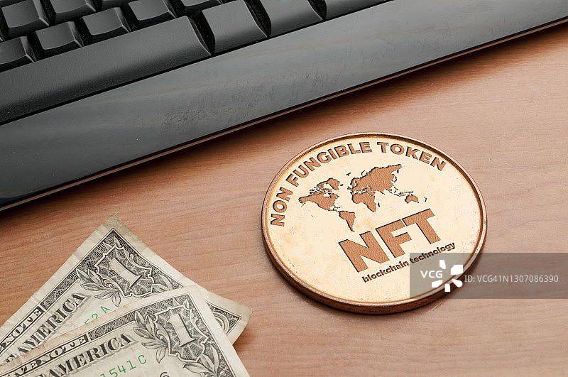 Nft(不可替代的代币)概念:在一张木桌上放一枚大铜币，上面有电脑键盘和两美元钞票图片素材