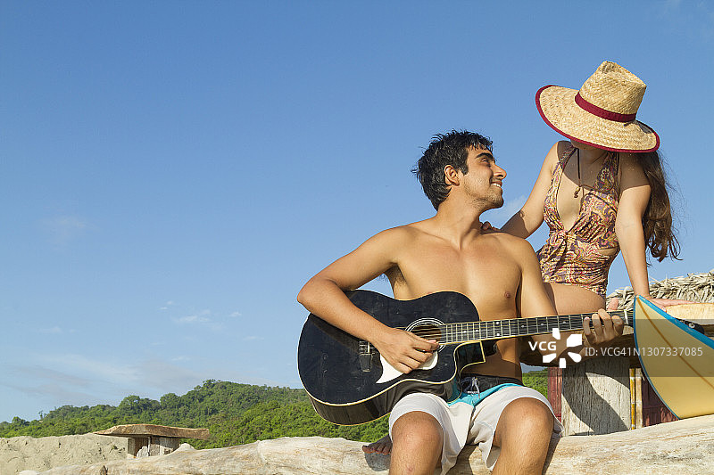 一对拉丁健美的异性恋冲浪者夫妇，在大海前弹奏原声吉他，放松在卡诺阿，Manabi省，厄瓜多尔，拉丁美洲图片素材