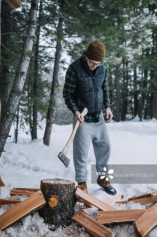 一个戴着无檐帽和法兰绒的男人在雪地里砍柴图片素材