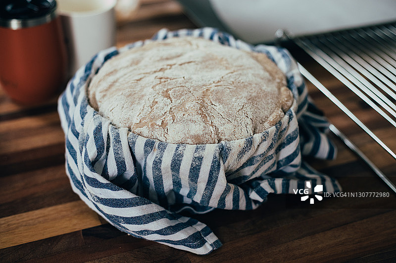 传统家庭制作的酸面包，在烘烤前在厨房用茶巾盖在篮子里图片素材