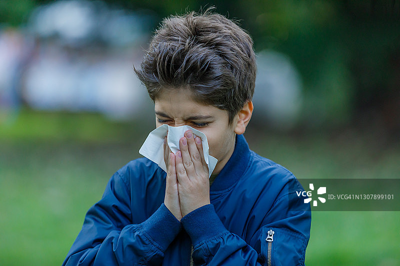 一个患季节性流感的男孩在公园里散步，用纸巾咳嗽。图片素材