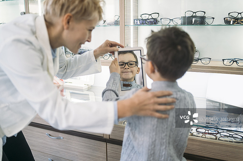 微笑的男孩，看着镜子里的自己，展示他的新眼镜图片素材