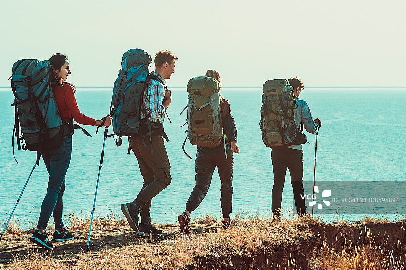 四个背着背包的旅行者沿着海岸行走图片素材