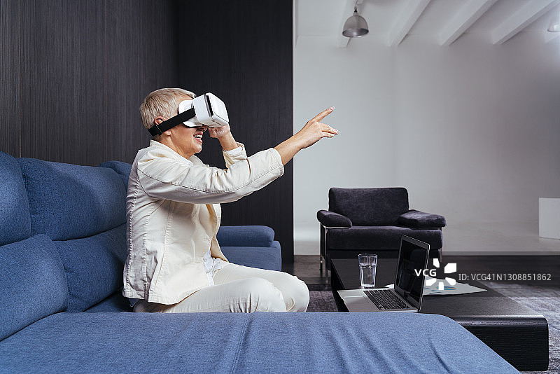 资深女商人在沙发上用虚拟现实耳机打手势图片素材