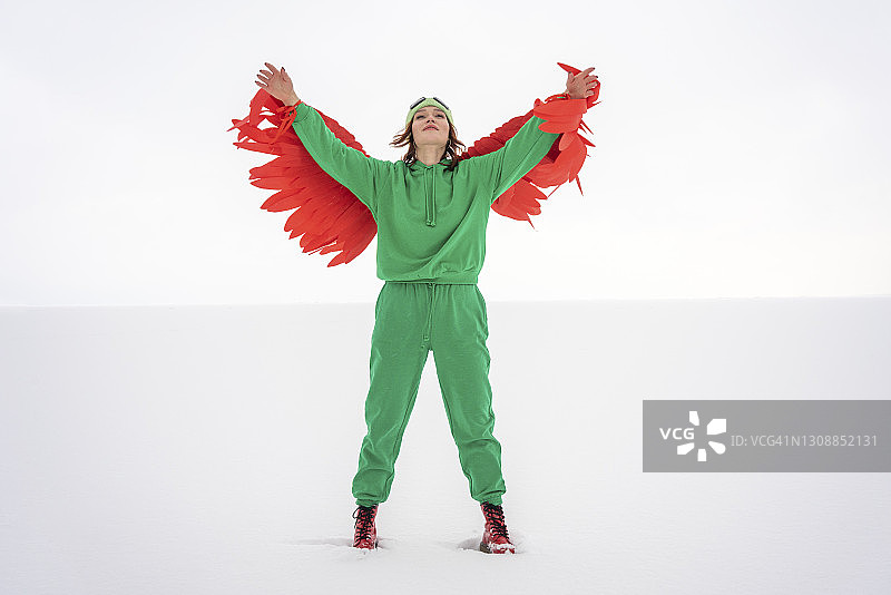无忧无虑的女人在绿色的鸟服装举起手臂，而站在雪地上对着天空图片素材