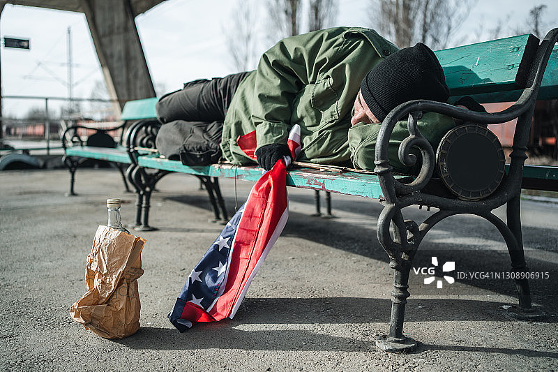 无家可归的退伍军人拿着美国国旗睡在长凳上图片素材