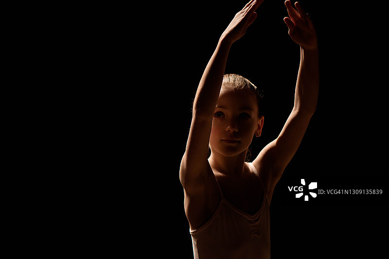 一个年轻的芭蕾舞者在黑色背景上摆姿势。图片素材