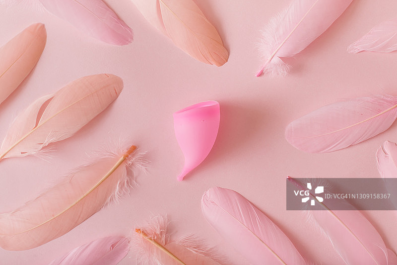 粉色背景上的月经杯和羽毛。俯视图，平放图片素材