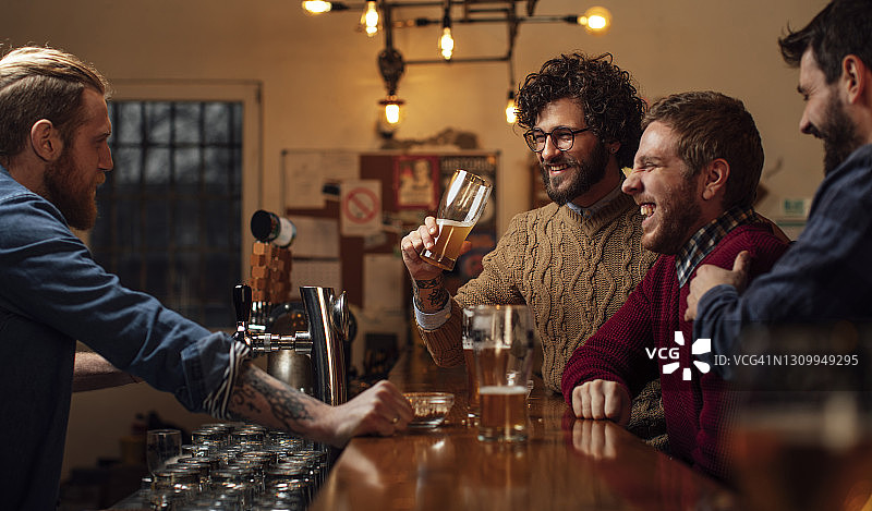 一群朋友在酒吧里喝着啤酒，和酒保一起笑图片素材