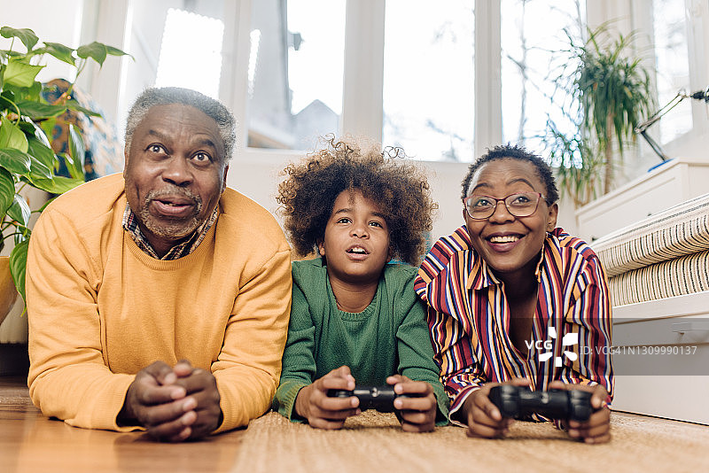 一对非裔美国老年夫妇和他们的孙女躺在地板上玩游戏图片素材