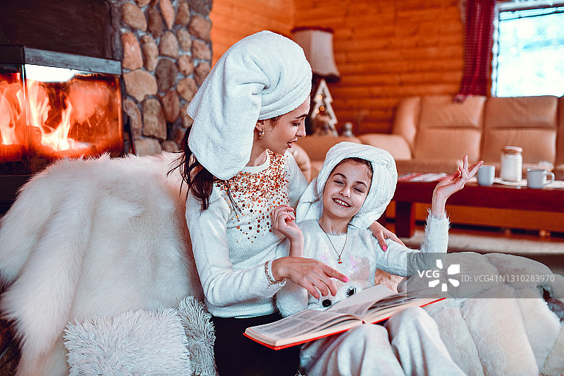 母亲和女儿洗澡后在小屋壁炉旁阅读童话书的时间图片素材