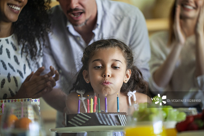 小女孩吹蜡烛的生日蛋糕，她的家人唱歌的背景图片素材