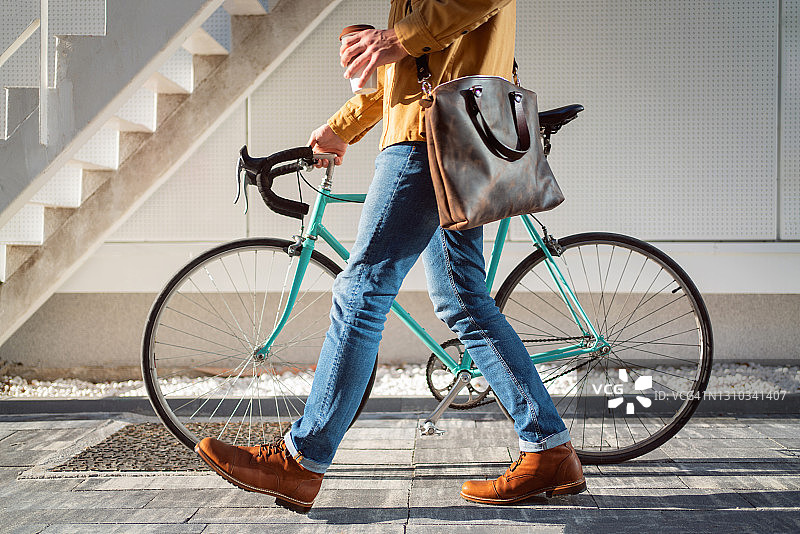 侧视图，一个不认识的现代男人与他的自行车，而携带一杯咖啡图片素材