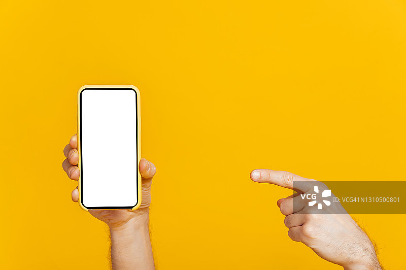 触屏智能手机，手机用空白白屏幕呈现在男性手中，手指指向手机，在孤立的橙色背景，复制空间，模型概念图片素材