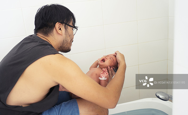 亚洲年轻的成年父亲在家里的浴室里为他的小女儿洗澡图片素材