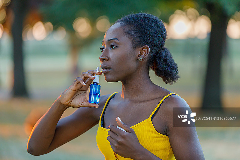 一位非裔美国妇女在户外过敏并使用哮喘吸入器。图片素材