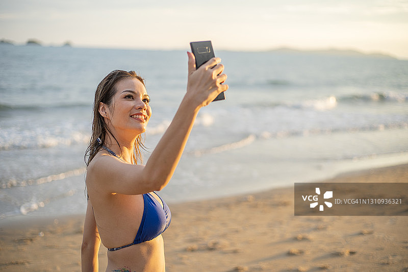年轻女性在海滩上自拍和视频电话与比基尼。图片素材