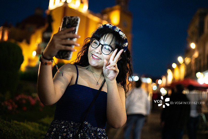 一个女孩在街上用智能手机视频通话时做和平手势图片素材