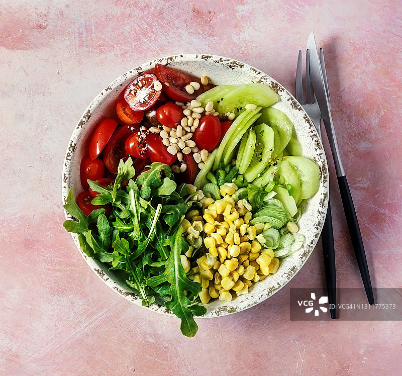 鲜食材(芝麻菜、番茄、黄瓜和玉米)放在一个粉红色背景的碗里图片素材