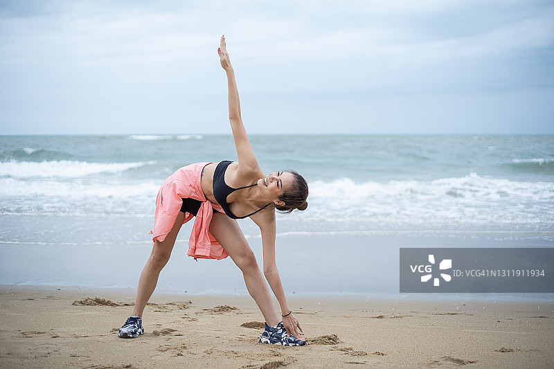 快乐的运动女性在海滩锻炼前伸展图片素材
