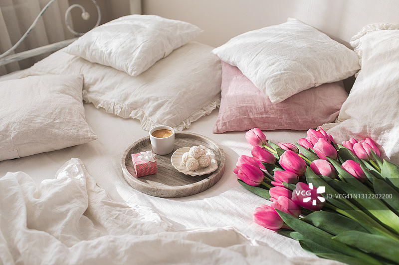 托盘上的咖啡，candyâs和礼品盒与一束郁金香在白色的亚麻床上。图片素材