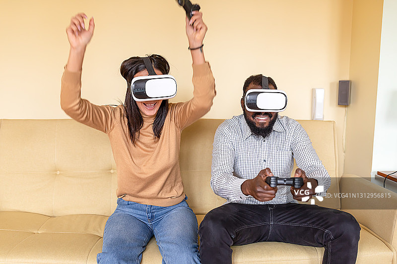 高兴的非裔美国人和他的中国女友在家里用VR玩电子游戏。图片素材