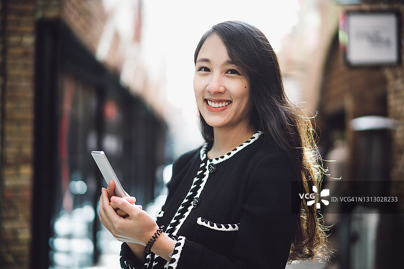 一个快乐的亚洲女人拿着智能手机站在购物中心的肖像图片素材