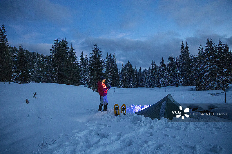 游客在冬山露营时，夜间在帐篷附近使用手机。在2019冠状病毒病大流行期间，自然是孤独的。心理健康和生活平衡。图片素材